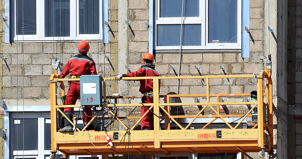 Workers on a suspended scaffold mount fasteners for a rainscreen.