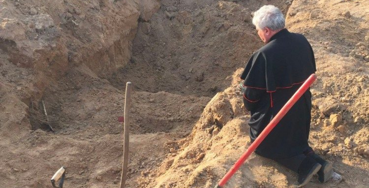 Cardeal Konrad Krajewski reza ao lado de uma fossa comum em Borodjanka, Ucrania Foto Vatican Media