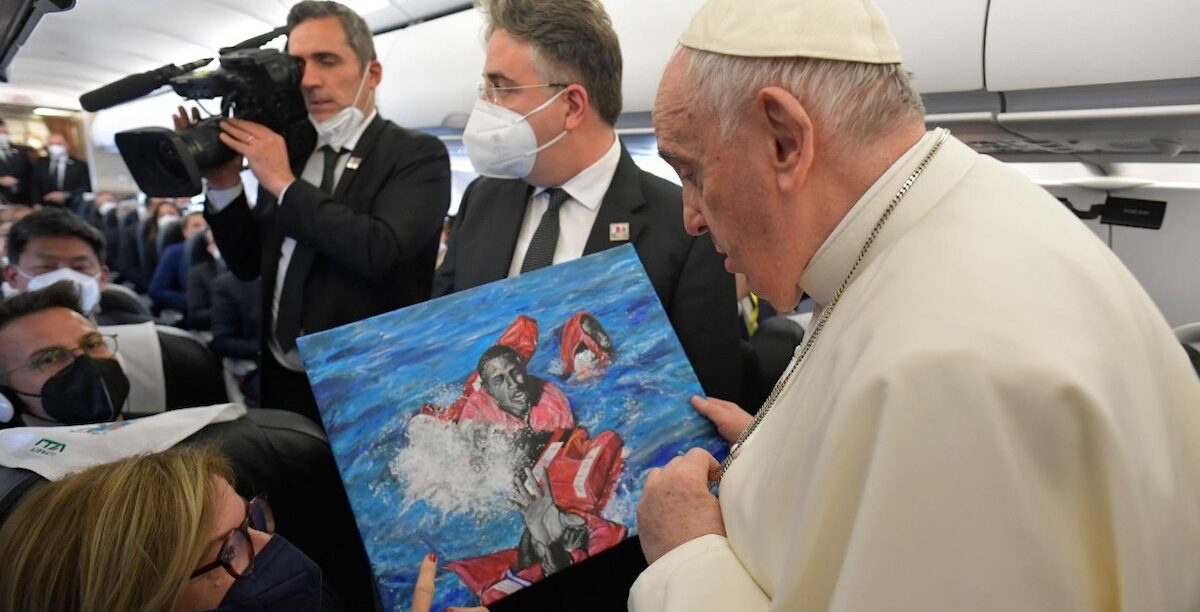 Papa Francisco, Malta, Ucrânia, refugiados O Papa Francisco, no voo para Malta (2 Abril 2022), ao receber um quadro, pintado por Daniel Jude Okeoguale, refugiado com quem se encontrará durante a viagem ao país, dia 3 Abril. Okeoguale sobreviveu a um naufrágio, no Mediterrâneo, e evoca na obra todos os que morreram na mesma viagem e ele não conseguiu salvar. Foto © Vatican Media.