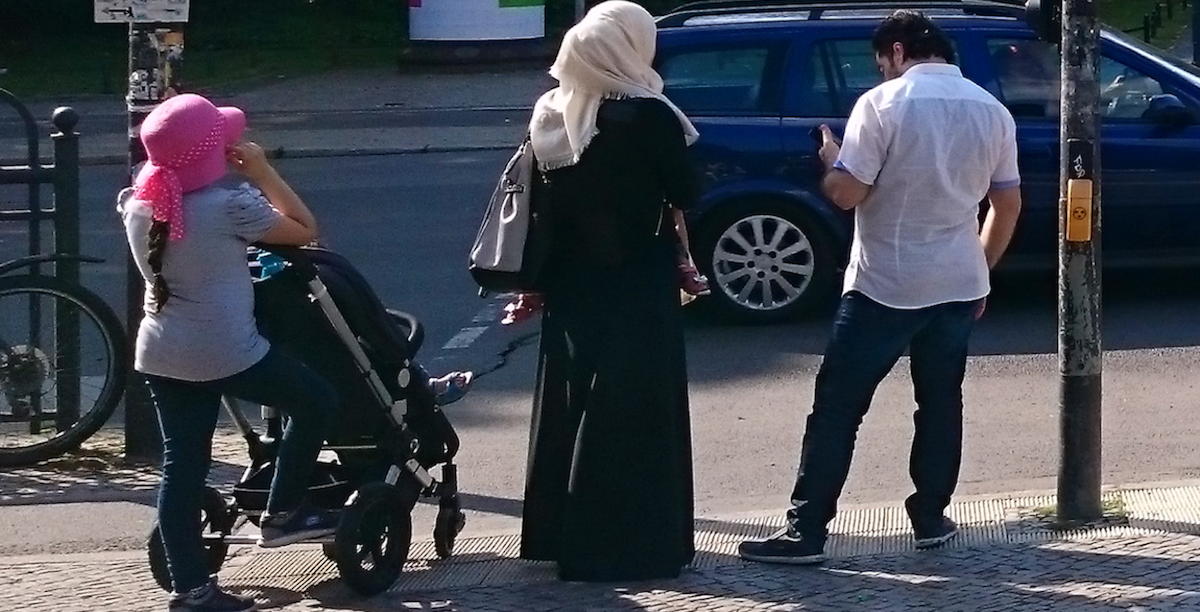 1280px-Islamische-familie-frau-abaya-kopftuch-hidschab_20170721 Família muçulmana nas ruas de Berlim (Alemanha). A mulher veste uma abaya, uma longa túnica, e cobre a cabeça com um véu. Nas escolas francesas, o véu já está proibido desde 2004, agora a proibição vai estender-se ao vestido. Foto © hilmar h. werner, Copyrighted free use, via Wikimedia Commons.