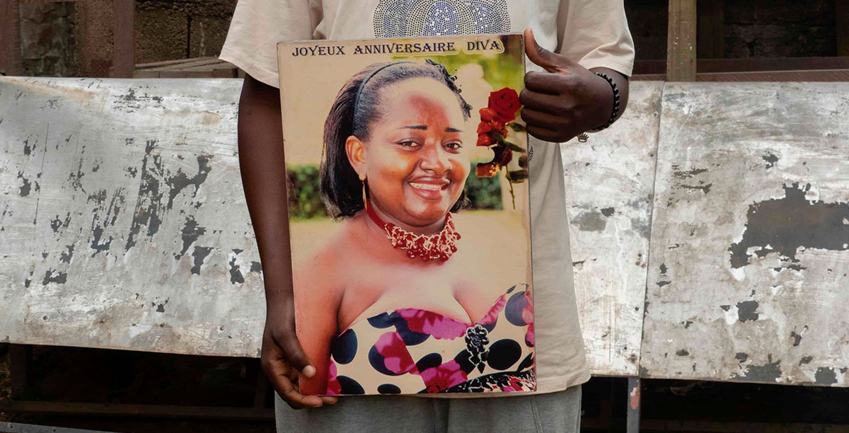 O filho de Dorgelesse Nguessan, Lontchi Jean Oki, segura uma fotografia da mãe na casa da família em Douala, Camarões, a 7 de julho de 2022. Foto © Amnesty International