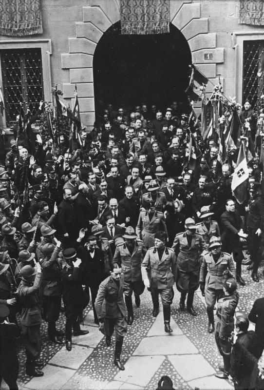 O ditador italiano Mussolini, acompanhado pelos seus apoiantes na Praça da Catedral de Milão, em maio de 1930. Bundesarchiv, Bild 102-09843 / CC-BY-SA 3.0, CC BY-SA 3.0 DE <https://creativecommons.org/licenses/by-sa/3.0/de/deed.en>, via Wikimedia Commons