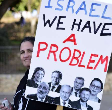 Mulher com cartaz contra vários líderes políticos israelitas. Foto DR via JPR 1