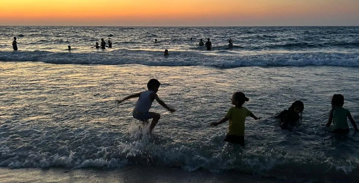 Apesar de tudo, crianças brincam nas ondas da costa da Faixa de Gaza durante a devastadora guerra de um ano de Israel. Foto Nour ElAssyTNH