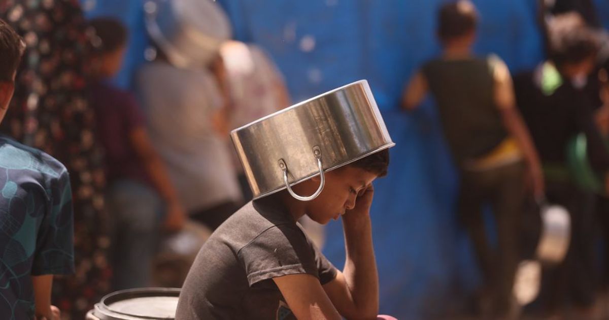 UN News Uma criança colocando uma panela na cabeça para se proteger do sol enquanto espera para conseguir comida