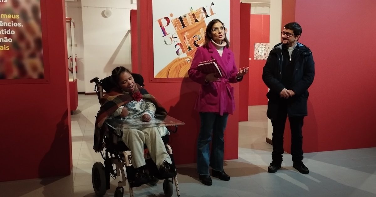 Antónia Neves, uma pessoa não verbal e com dificuldades motoras, Maria Serrano, a sua educadora social que a acompanha há 25 anos, e pe. Simão Pedro, na inauguração da mostra. Foto: Direitos reservados.