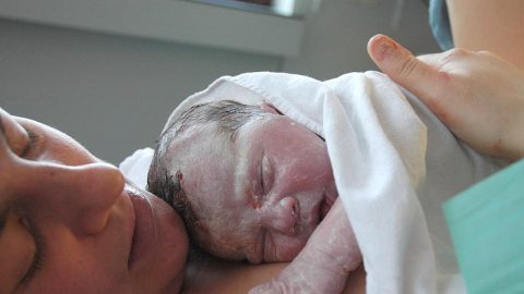 Bebé na barriga da mãe logo após o nascimento, com a pele coberta de vérnix e um pouco de sangue. Falar de violência obstétrica não significa negar os progressos clínicos nem desvalorizar a complexidade técnica do parto. Foto © Tom Adriaenssen, CC BY-SA 2.0 , via Wikimedia Commons.