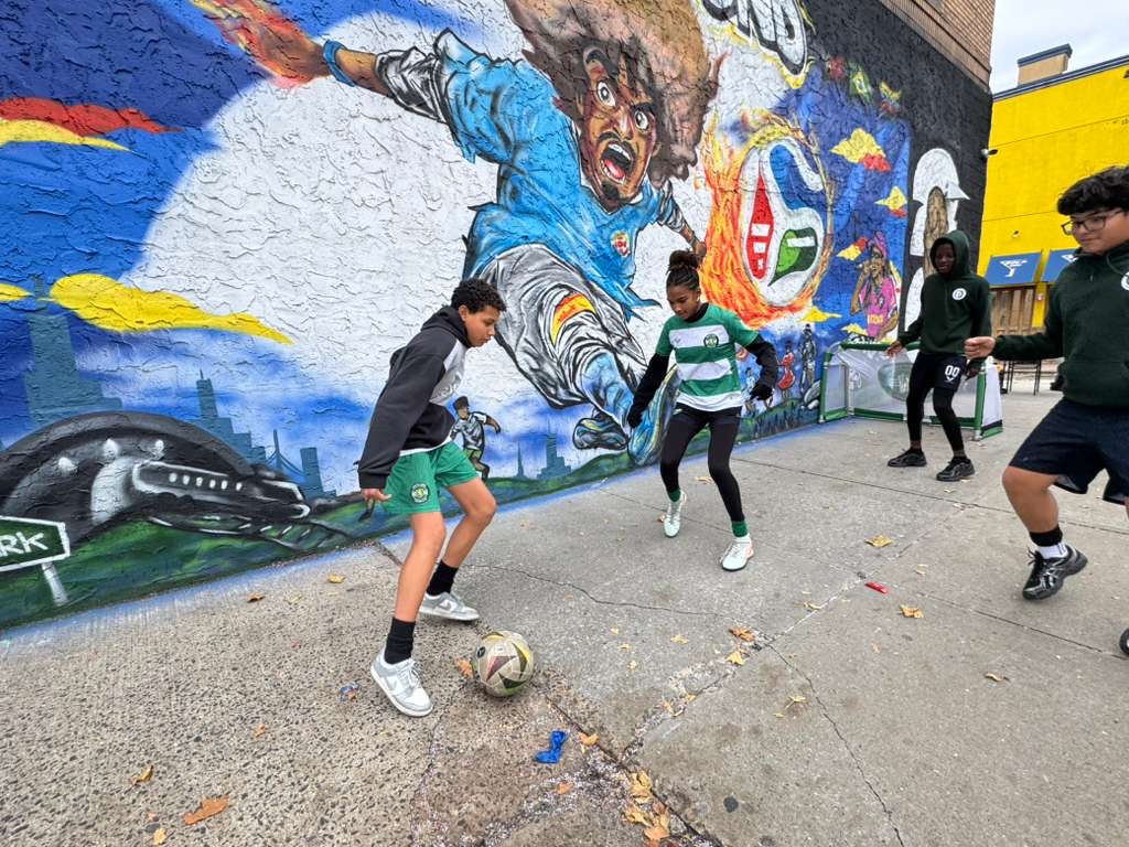 Crianças de Newark a jogar futebol em frente ao mural do World Cup Corner - Unicorn151. WikiWashyy, CC BY 4.0 , via Wikimedia Commons EUA campeonato mundial futebol