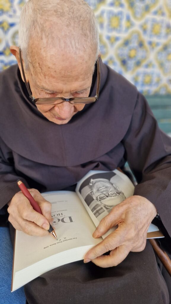 O padre Rema assina o livro de memórias que os irmãos Franciscanos editaram pelo seu aniversário. Foto © Clara 
